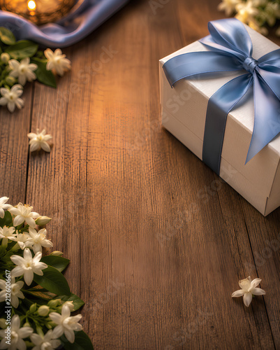 White gift box with a blue ribbon and fresh jasmine flowers on a rustic wooden table with copy space