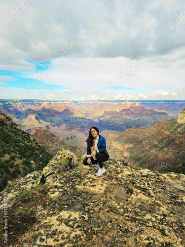 A beautiful young woman crouching on the edge of a rock in front of the American Grand Canyon National Park in Arizona, Usa.