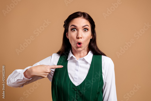 Foto Surprised young woman in green vest pointing at herself with shocked, wide-eyed