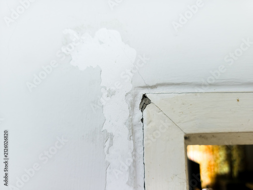 Damaged white wall with peeling paint and cracks around a wooden door frame corner
