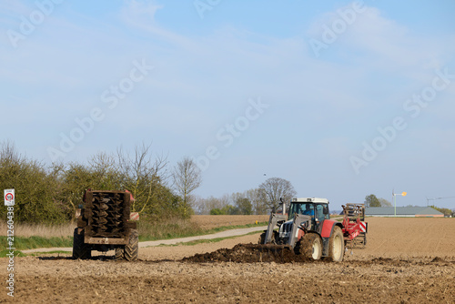Konstfotografi A red tractor plows a brown field, spreading rich manure