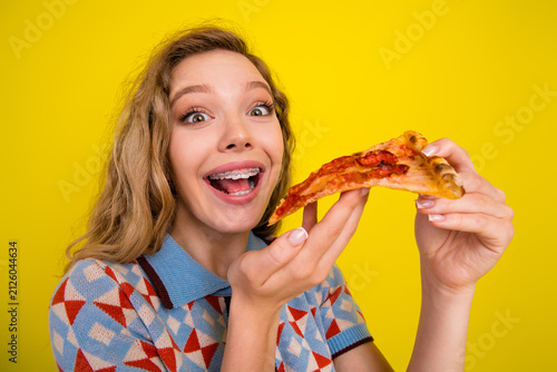 Принти на полотні Happy teenage girl with braces enjoying a slice of pizza against a bright yellow