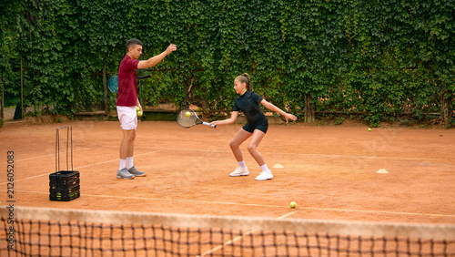 Canvastavla Young girl waits in ready stance as male tennis coach feeds ball during clay court lesson