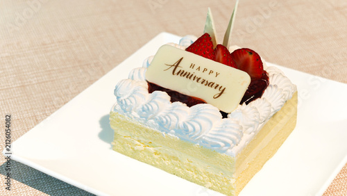 Elegant square anniversary cake with whipped cream frosting and fresh strawberries on white plate.