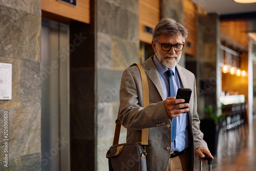 Mature hotel guest using smart phone app during his business trip.