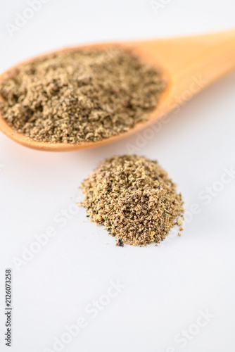 Fotografie Ground black pepper powder measured in a wooden spoon on white background