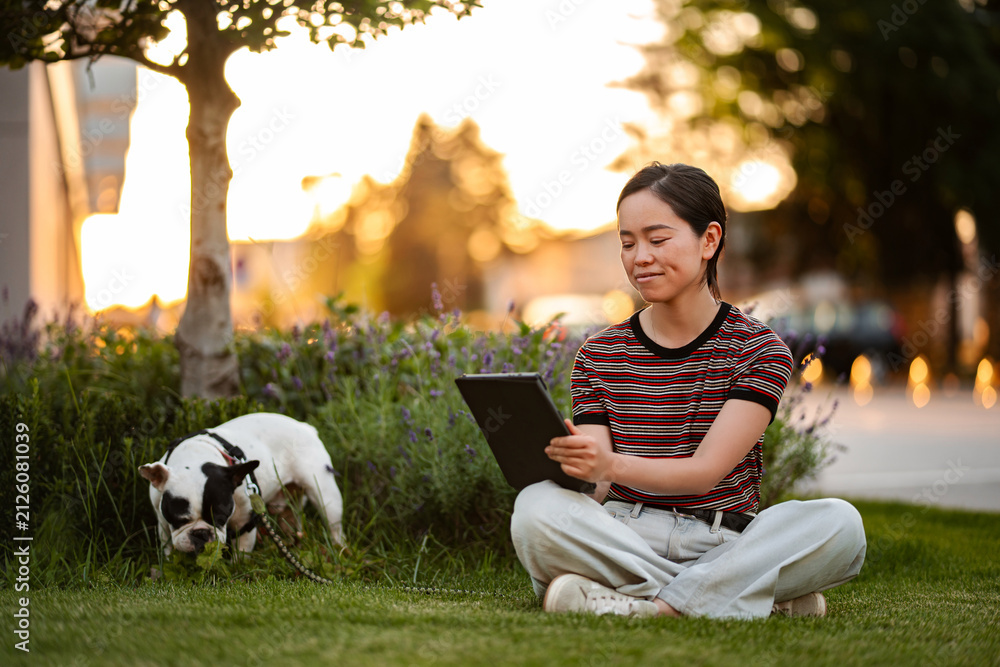Obraz premium Japanese woman using tablet in park with French bulldog