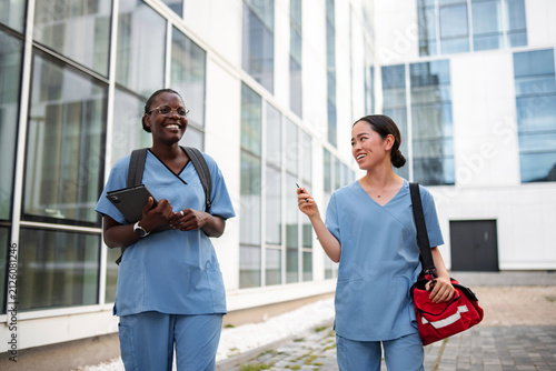 Diverse nurses walking enjoying conversation outside clinic building