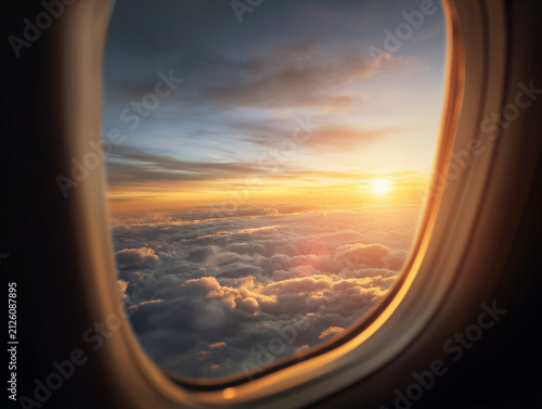 Airplane window view above the clouds with sunrise and aircraft wing during flight