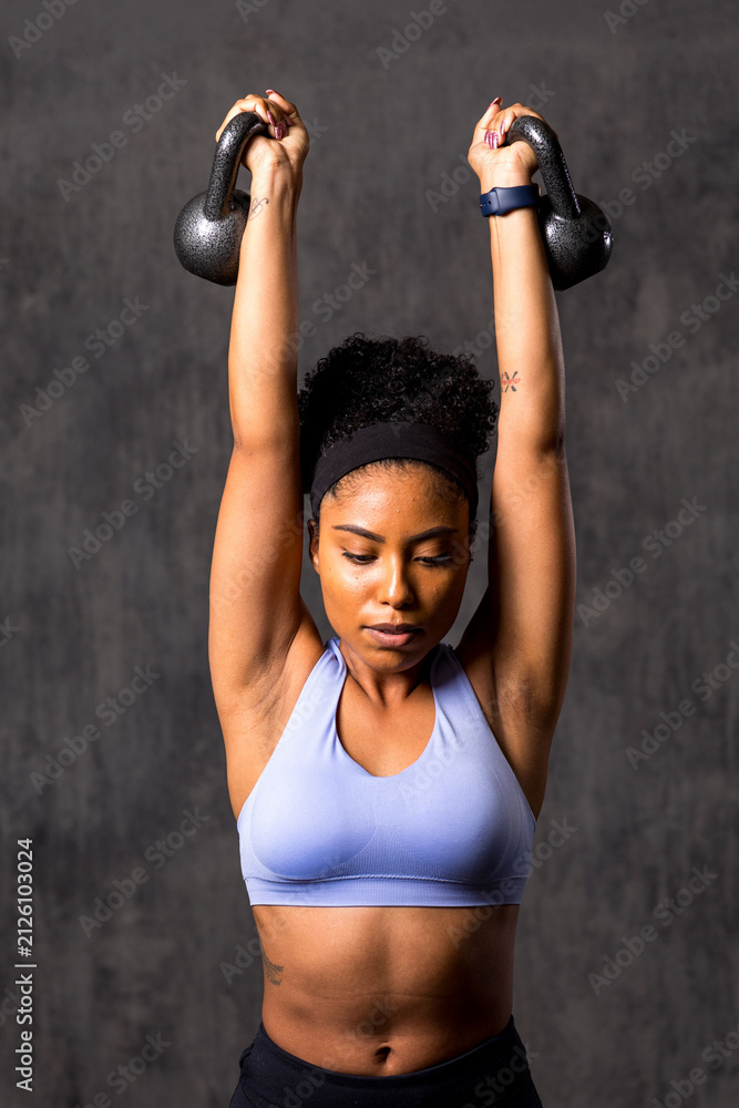 Fototapeta premium Focused woman lifting kettlebells powerfully.