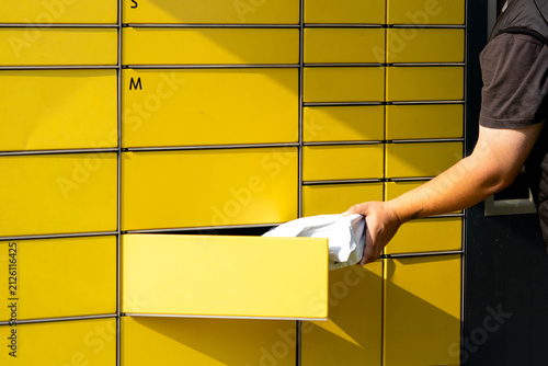 Person retrieving package from yellow delivery locker with multiple compartments in urban setting