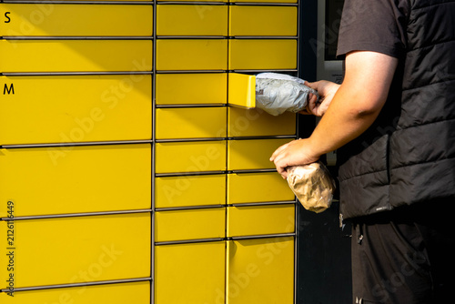 Individual retrieving packages from yellow parcel locker system in urban setting
