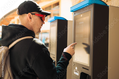 Side view of a millennial guy paying with screen terminal on a city street. Concept of urban automation, contactless payment, modern infrastructure, and self-service technologies.
