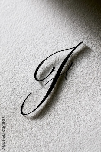 Close-up photograph of an elegant black cursive J hand-lettered on white textured paper