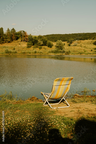 A stationary beach chair by the lakeside, featuring a relaxed atmosphere with yellow and gray upholstery.