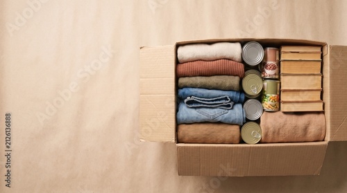 cardboard donation box filled with clothes, canned food, and books, soft natural window lighting, warm neutral color palette, clean empty space in the upper half for text
