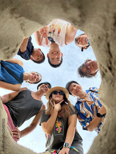 Asian multi generation family taking bottom up hole beach selfie on summer vacation, multi-generational Thai family with gen alpha kids smiling looking down at camera, happy creative holiday portrait.