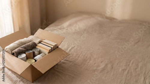 cardboard donation box filled with clothes, canned food, and books, soft natural window lighting, warm neutral color palette, clean empty space in the upper half for text