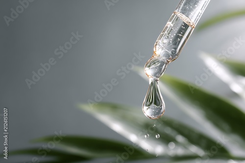 Close-up of a pipette with a drop of liquid and green leaves, conveying purity and natural essence.