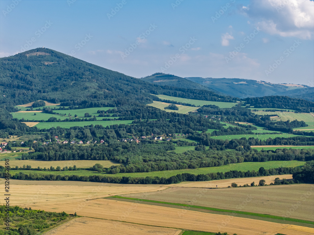 Obraz premium Aerial drone view of Biskupia Kopa mountain in the Opawskie Mountains, Poland, during summer, showing surrounding agricultural fields, forests and picturesque countryside landscape of Sudetes region
