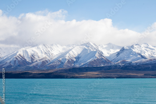 Snow covered mountain range above turquoise alpine lake under dramatic clouds