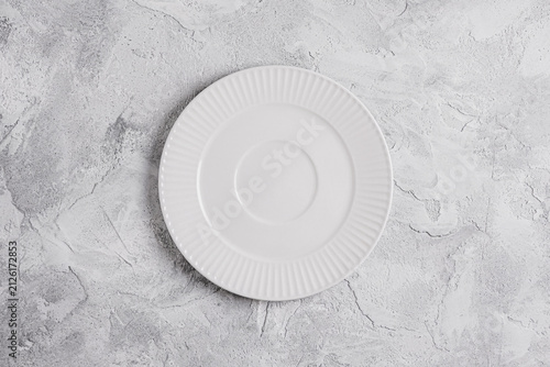 Empty white ceramic plate on a light gray decorative plaster background with copy space. Minimal table setting for food presentation, menu design, recipes, restaurant branding and culinary mockups.