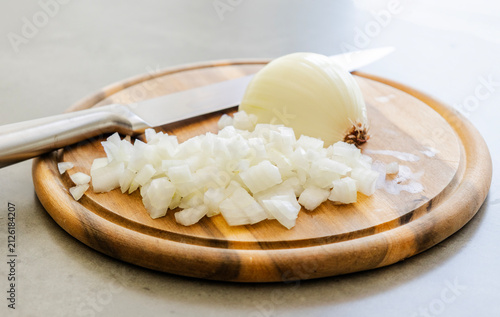 Chopped White Onion and Chef Knife on Round Wooden Cutting Board Close Up