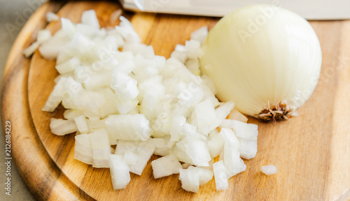 Chopped White Onion and Chef Knife on Round Wooden Cutting Board Close Up