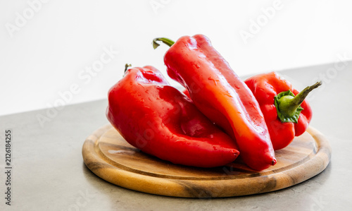 Whole Washed Red Paprika Peppers Stacked on Wooden Cutting Board