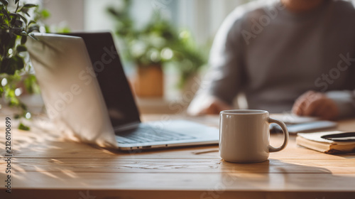 Freelancer working on laptop with coffee at wooden table. Remote worker using notebook computer for business tasks in cozy home office.