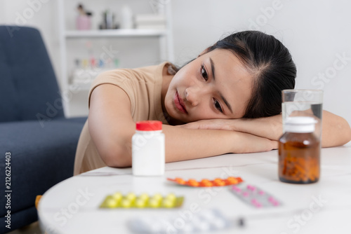 Canvastavla Sad asian woman feeling sick resting head on white table looking tired at medici