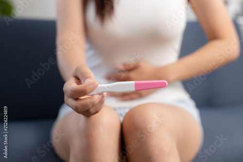 Quadro su tela anxious woman holding pregnancy test in her hand while sitting on blue couch at