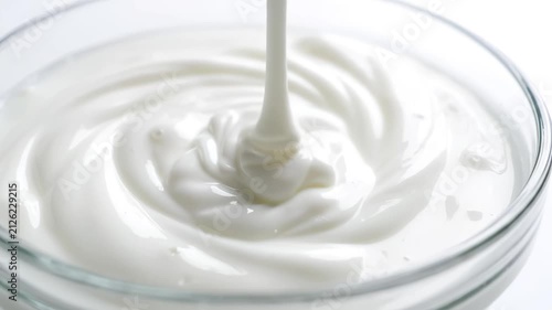 Creamy yogurt being poured into a glass bowl, creating elegant swirls on white background, close-up macro shot