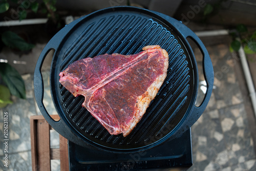 Man grilling a porterhouse steak over cast iron griddle, the smoke is visible through the high-heat sear, suitable for summer grill theme	