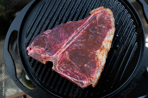 Man grilling a porterhouse steak over cast iron griddle, the smoke is visible through the high-heat sear, suitable for summer grill theme	