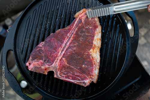 Man grilling a porterhouse steak over cast iron griddle, the smoke is visible through the high-heat sear, suitable for summer grill theme	