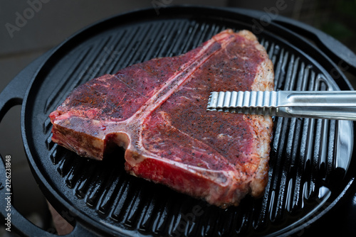 Man grilling a porterhouse steak over cast iron griddle, the smoke is visible through the high-heat sear, suitable for summer grill theme	
