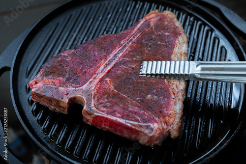 Man grilling a porterhouse steak over cast iron griddle, the smoke is visible through the high-heat sear, suitable for summer grill theme	