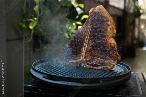 Man grilling a porterhouse steak over cast iron griddle, the smoke is visible through the high-heat sear, suitable for summer grill theme	