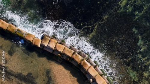 Aerial view of waving hitting the sand bag on the coastline.