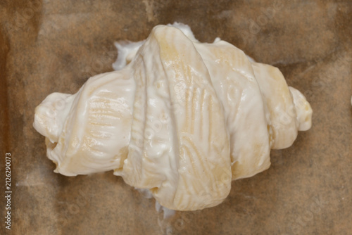 Fotografie Top view of an unbaked pastry croissant completely coated with thick white sugar glaze sitting on brown parchment paper