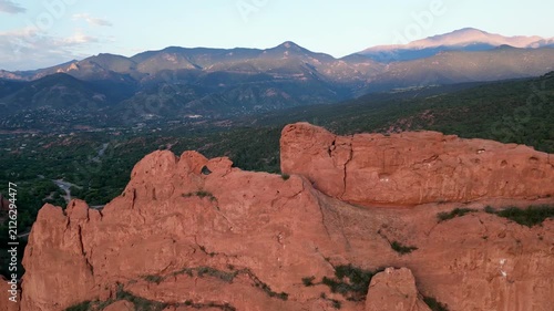 Aerial view flying parallel with large orange rock cliff with mountains in the background