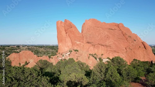 Drone rising up over tree to reveal big reddish orange rock formation in Colorado