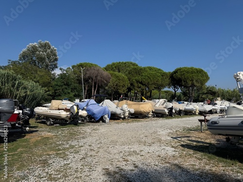 Bild auf Leinwand Wide view of outdoor boat storage yard with covered motorboats and inflatable boats on trailers under clear blue sky