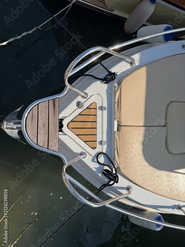 Top down close up of motorboat bow with stainless steel railing teak step pad and beige sundeck cushions. Marine detail highlights nautical design yachting equipment and boat maintenance.
