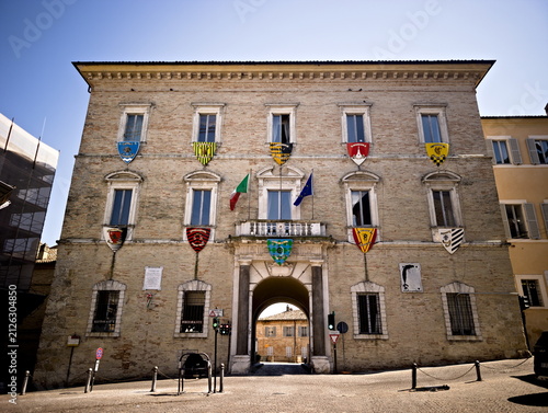 Facciata rinascimentale del Palazzo Comunale di Fermo, nelle Marche, decorata con le bandiere istituzionali e gli stemmi colorati delle storiche contrade cittadine della Cavalcata dell'Assunta