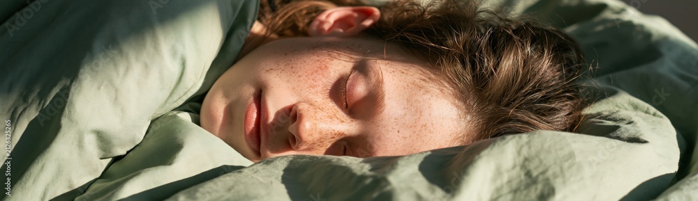Naklejka premium Closeup of sleeping woman with freckles in green bedding for bedroom background and wellness poster or relaxation wallpaper