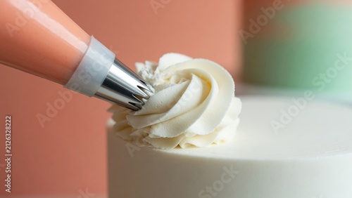 Pastry chef decorating white cake with delicate buttercream swirls using a piping bag and star nozzle, adding final touches