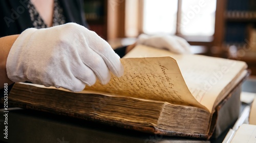 Hands in White Cotton Gloves Turning Page of Ancient Manuscript in Library Archive