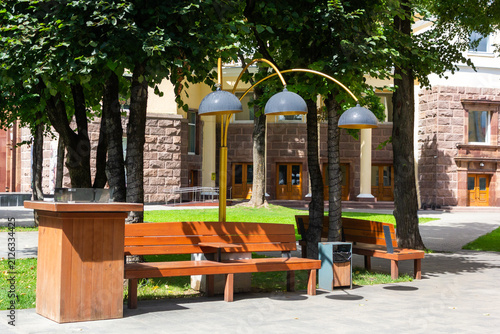 Wooden park benches next to a trash bin and decorative street lamps.